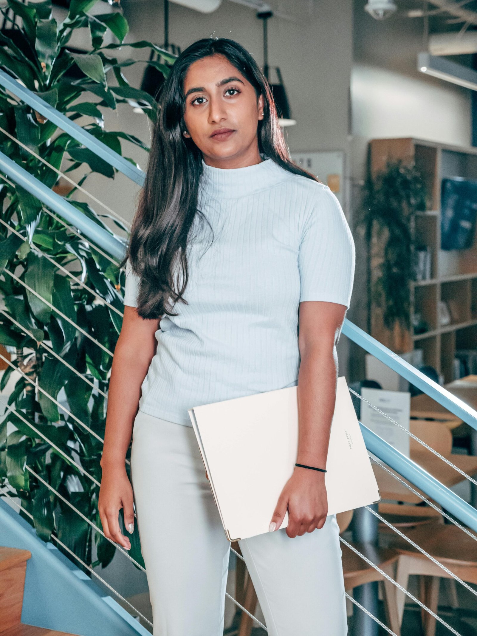 About Confident woman standing in a modern office with a laptop, exuding professionalism and focus.